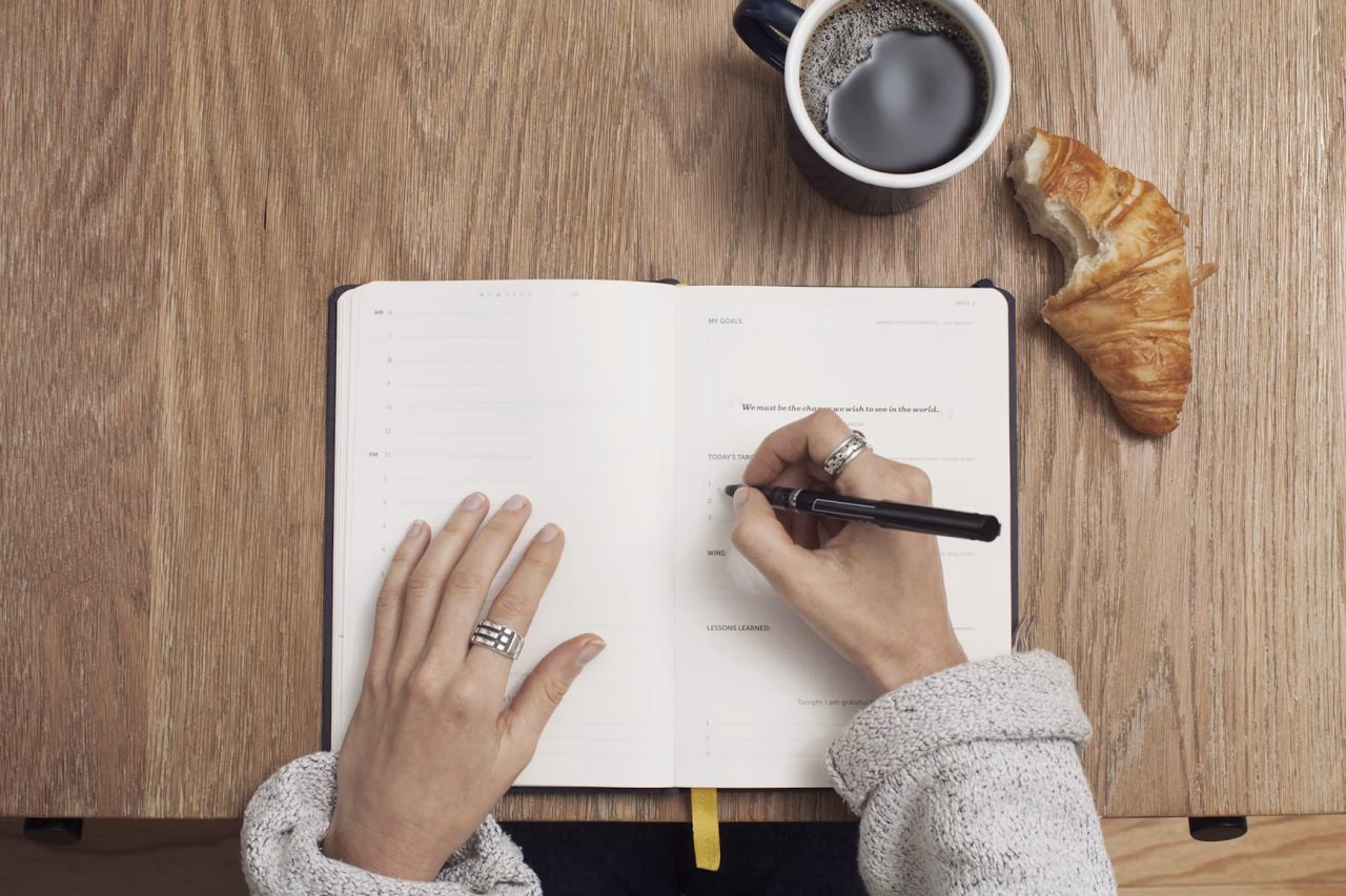 A person reviewing and writing in a diary beside coffee and breakfast